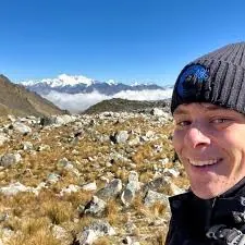 Max Adler, founder of Madler, smiling in a beanie with snow-capped mountains behind him